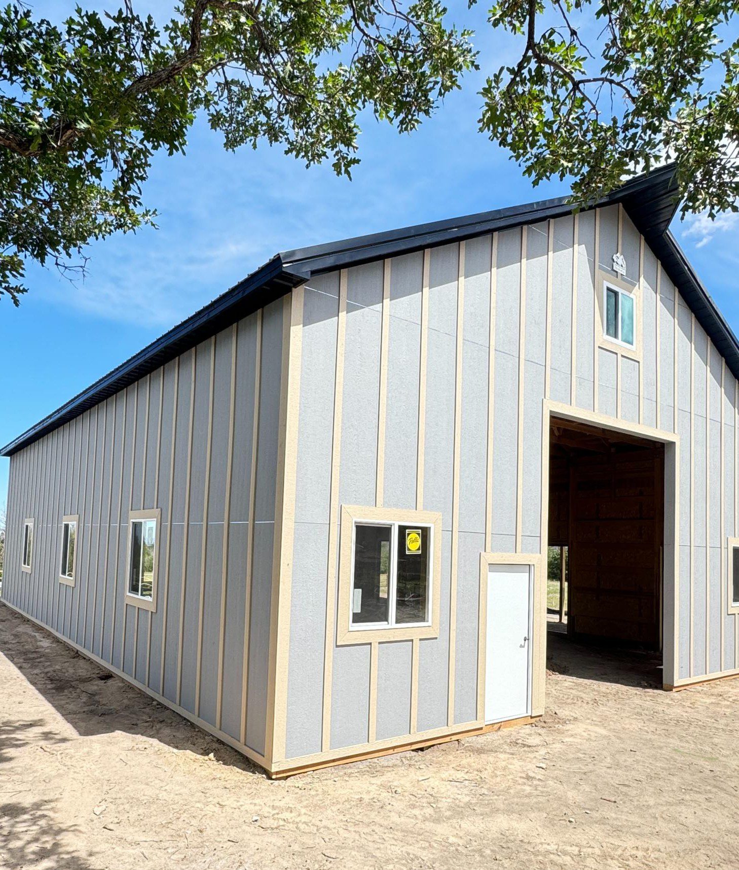 A large gray and beige barn-style building with a metal roof, multiple windows, and an open entryway under a blue sky.