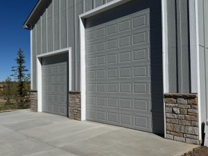Two large gray garage doors with stone accents on a modern building, shown on a sunny day with a clear blue sky.