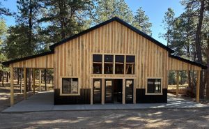A newly constructed wooden building with large windows and a covered porch, set in a pine forest.