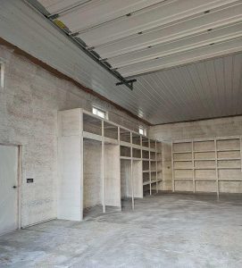 Empty garage with concrete floor, light-colored walls, and built-in shelving units along two walls under a partially open garage door.