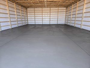 Interior of a large unfinished building with exposed wooden framing, white insulated walls, and a smooth concrete floor.