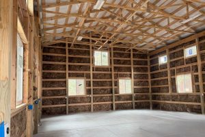 Interior of a partially constructed building with exposed wooden framing, insulation in the walls, several windows, and a concrete floor.