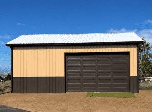 A beige and brown metal garage with a closed dark brown roll-up door, situated on a dirt lot with a small patch of artificial grass in front.