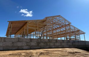 Partially built wooden frame structure of a building stands behind a concrete block wall under a clear blue sky.