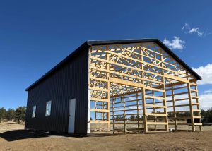 A half-built barn with dark metal siding on one side and exposed wooden framing on the other.