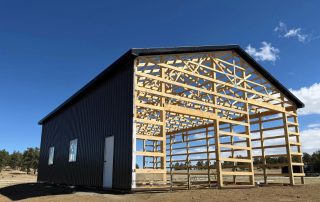 A half-built barn with dark metal siding on one side and exposed wooden framing on the other.