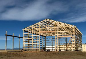Construction of a wooden-framed building against a blue sky with clouds.