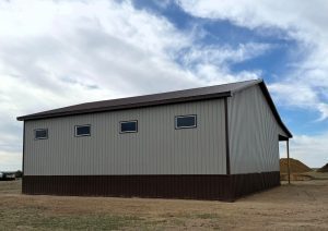A gray corrugated metal building with a brown roof and wainscoting. It has several rectangular windows.