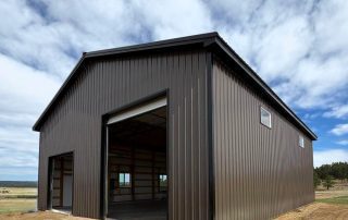 A brown metal barn with open garage doors under a cloudy blue sky.