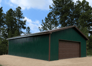 A green metal garage with a brown roll-up door sits on a gravel lot, surrounded by tall pine trees under a partly cloudy sky.