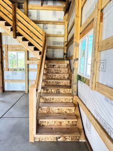 Unfinished wooden staircase in a building under construction, with exposed framing, OSB steps, and partially installed walls.
