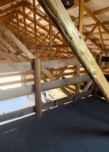 Interior view of a wooden loft with exposed beams, a partial railing, and a clock visible at the top, looking down toward a lower level.