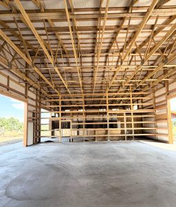 Interior view of a large unfinished building with exposed wooden beams and framework, concrete floor, and open walls.