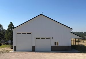 A white metal building with two large garage doors and a small window, set on a gravel lot under a clear sky.
