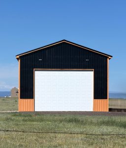 A black and orange building with a large white garage door stands on grass under a clear blue sky.